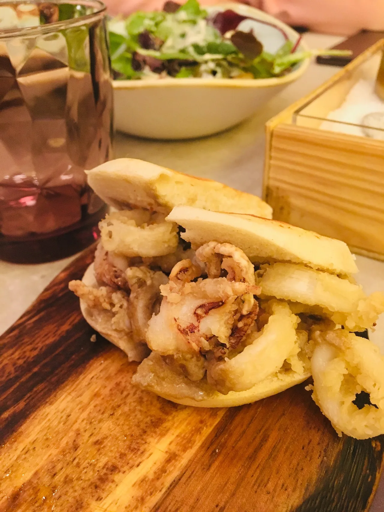A fried squid sandwich in a white bun on a wooden board
