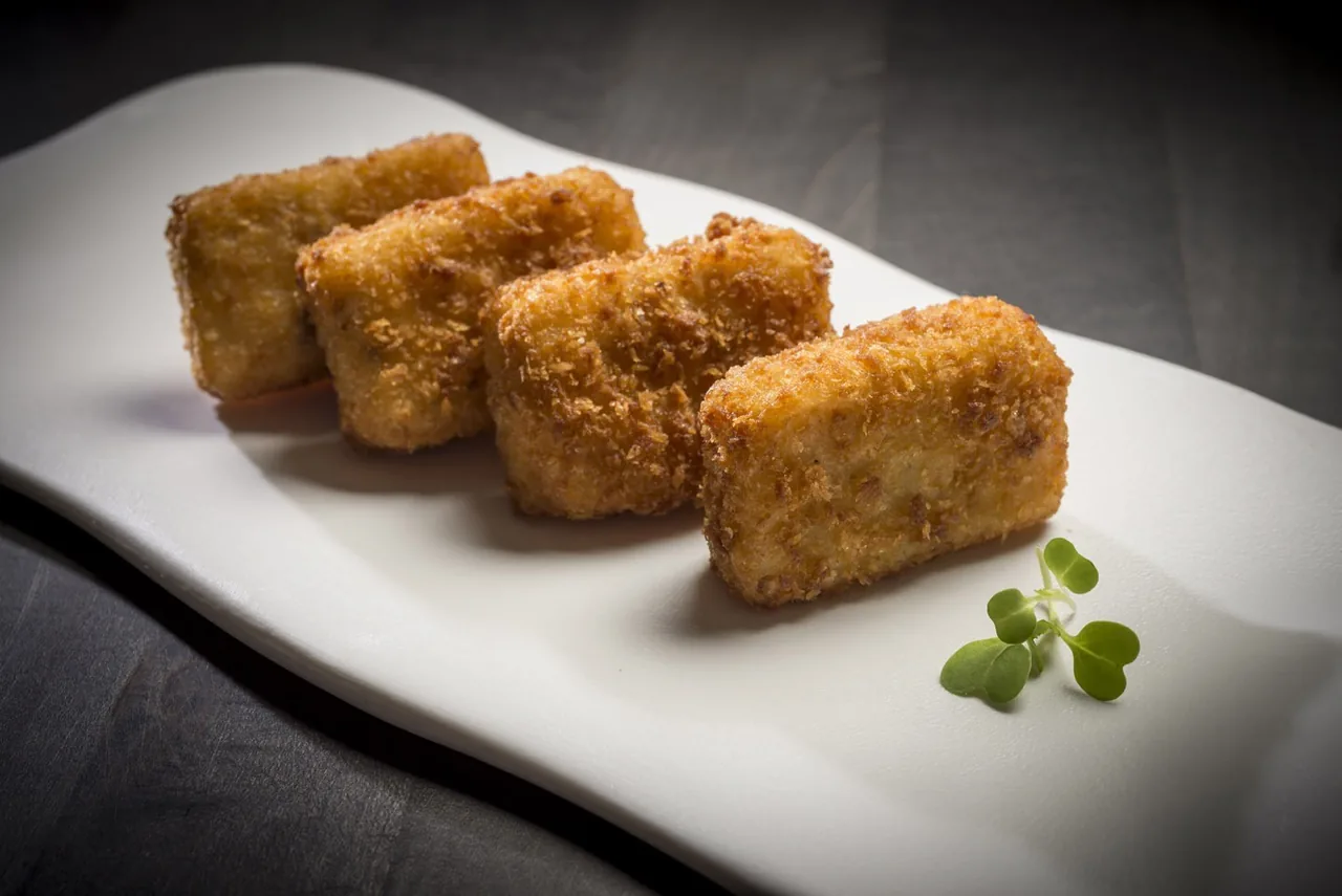 Four golden croquettes on a long white plate with a small herb sprig