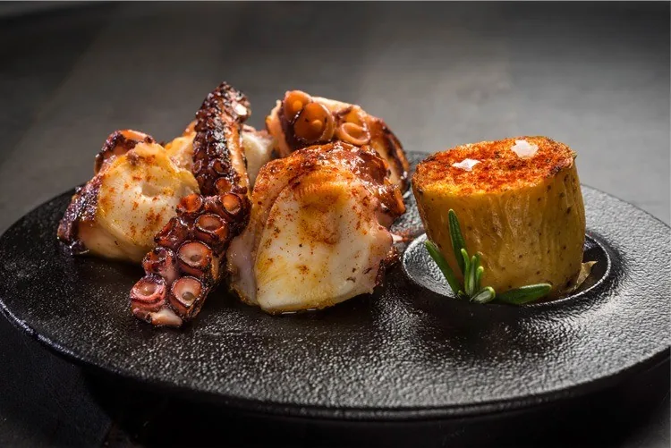 Grilled tentacles and a small golden round portion on a dark plate