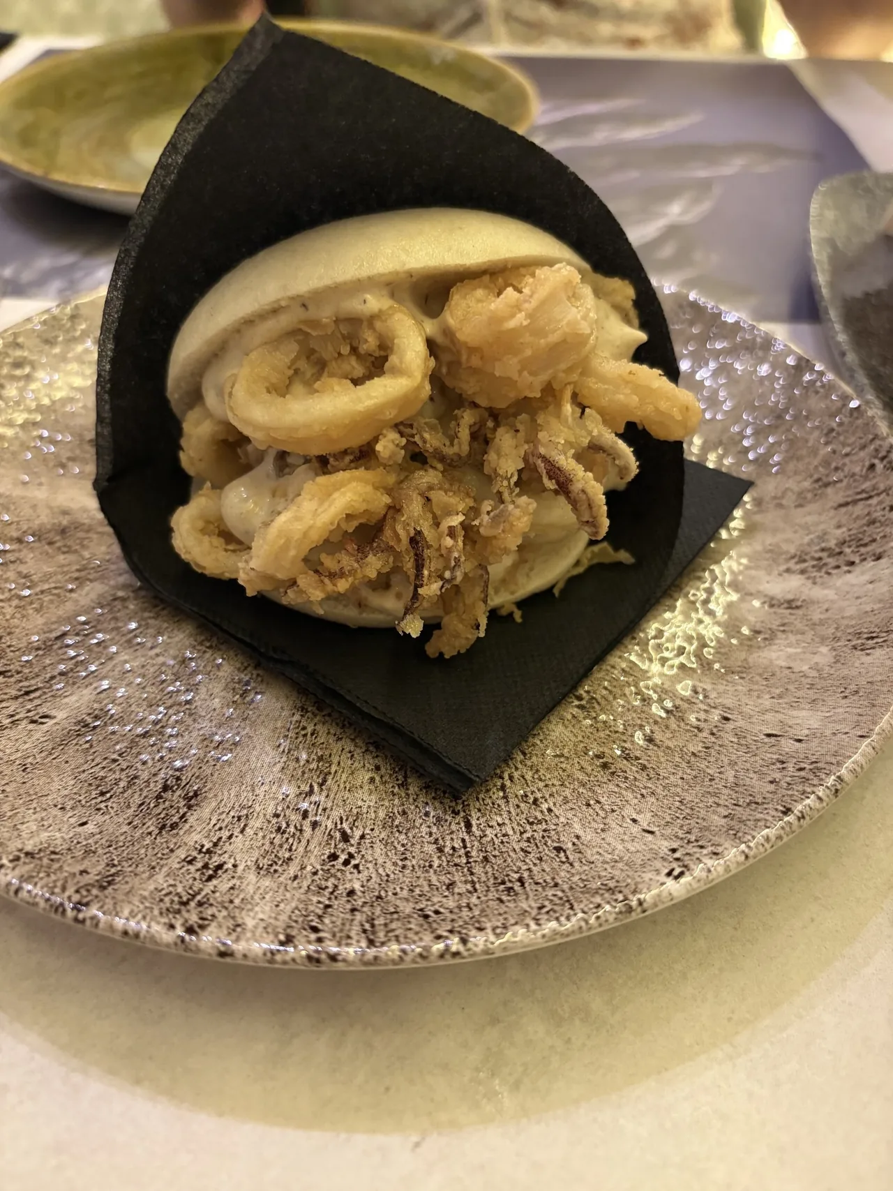 Fried squid tucked into a black steamed bun on a speckled plate