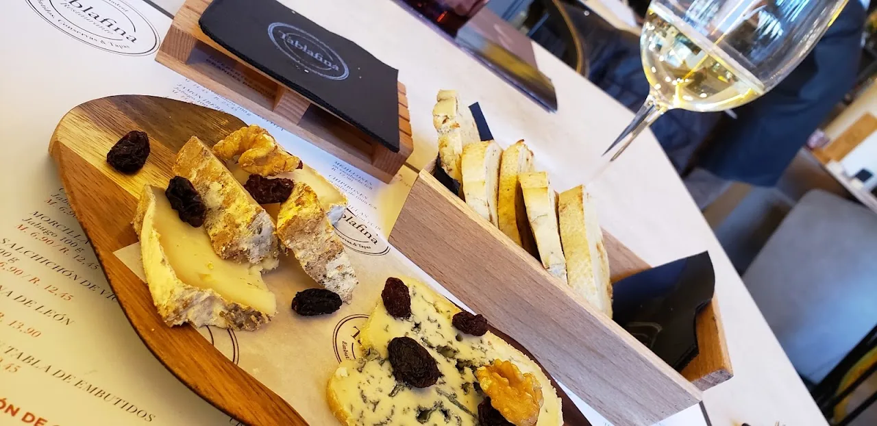A wooden board with sliced cheese, bread, and dried figs