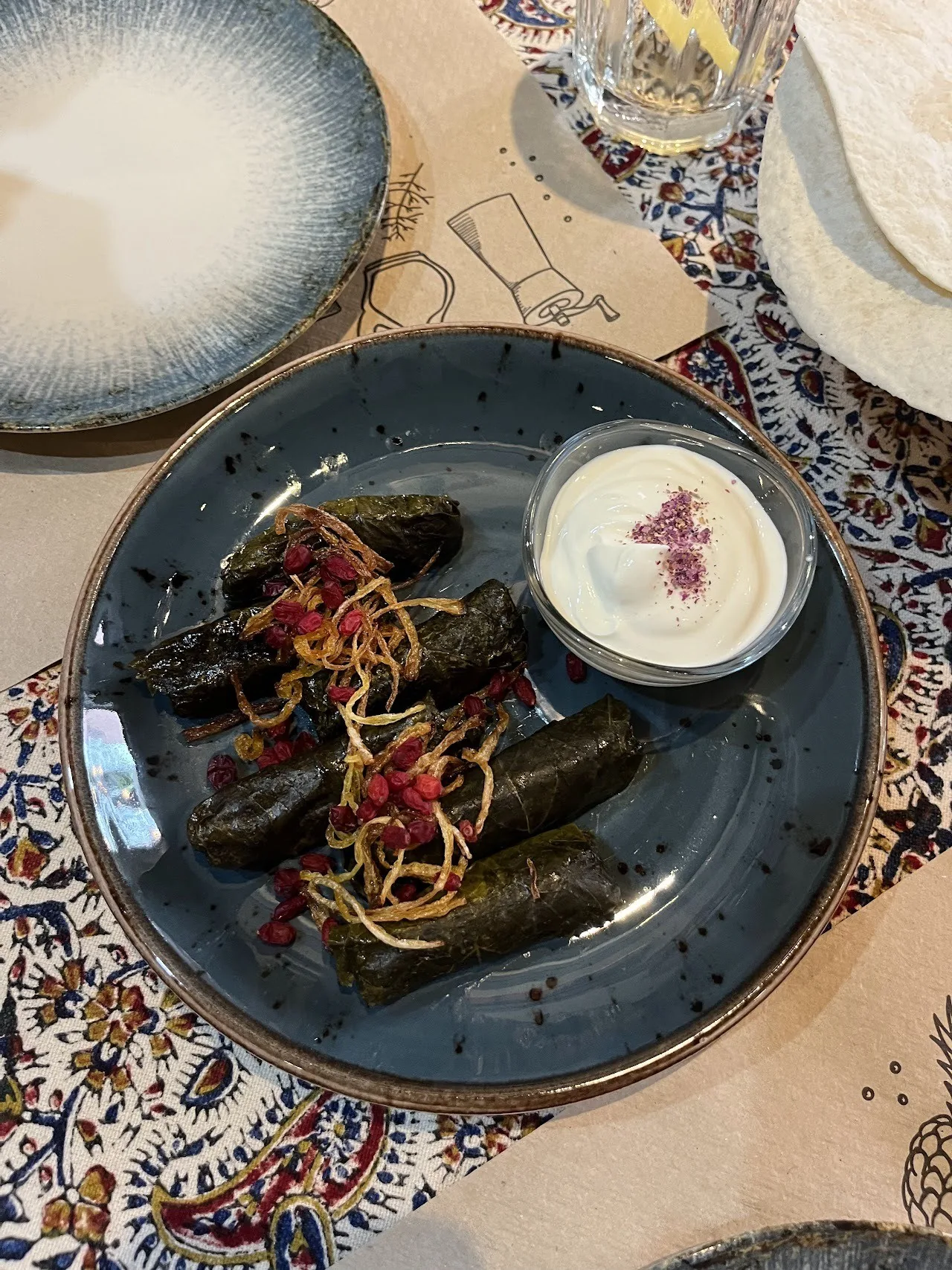 Stuffed vine leaves on a dark plate with a small bowl of white yoghurt
