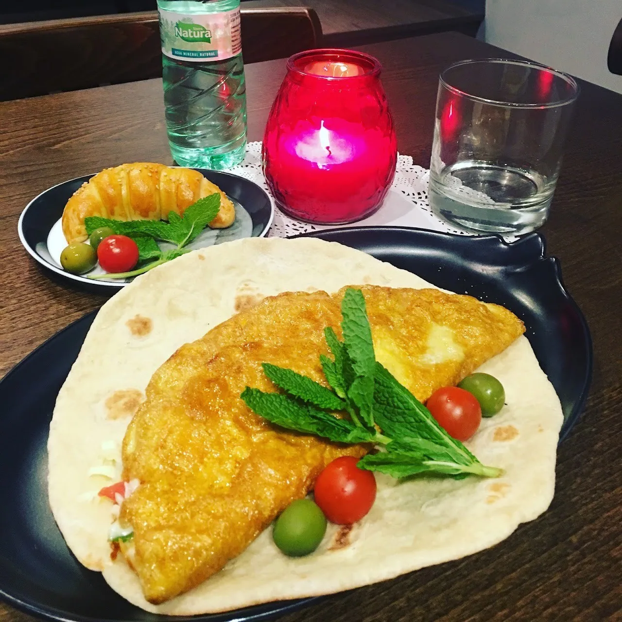 A folded flatbread omelette with fresh herbs and cherry tomatoes beside a small side plate