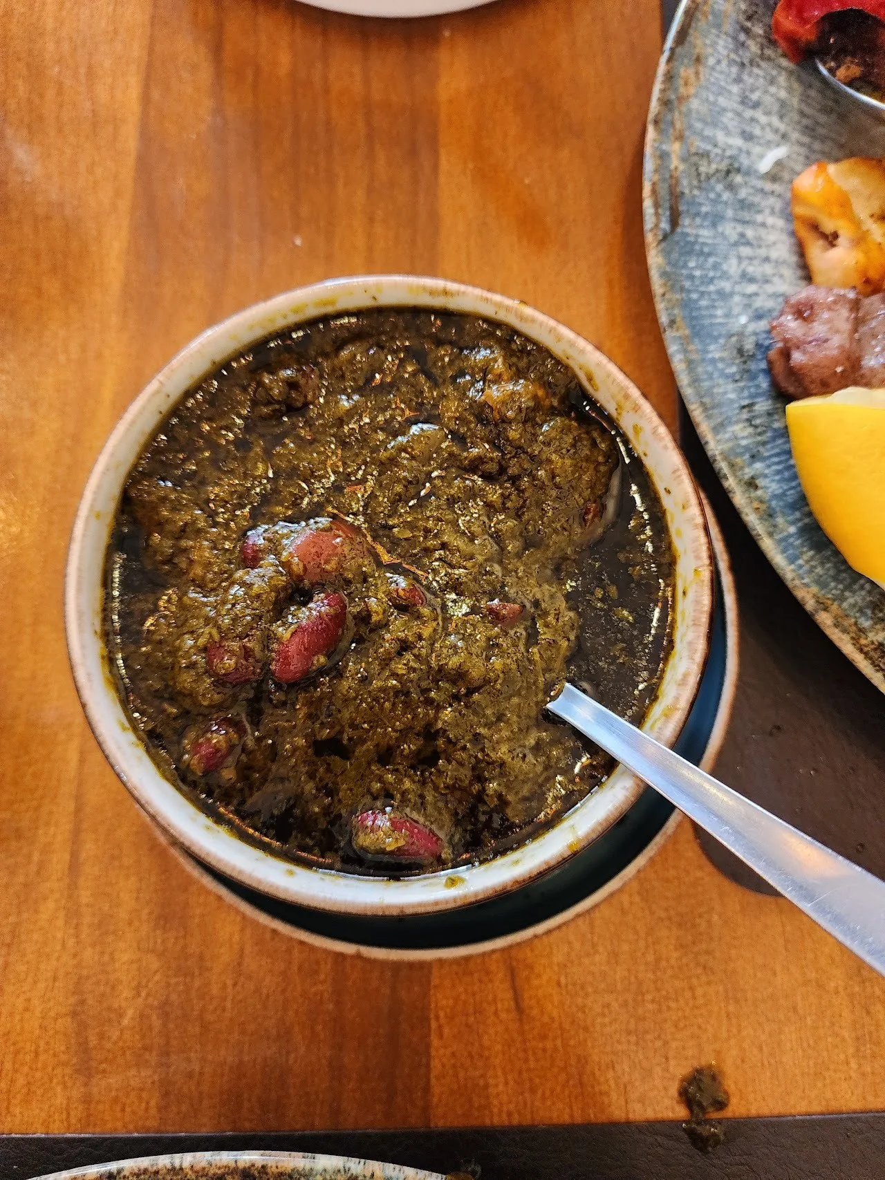 A bowl of dark green herb stew with a spoon on a wooden table
