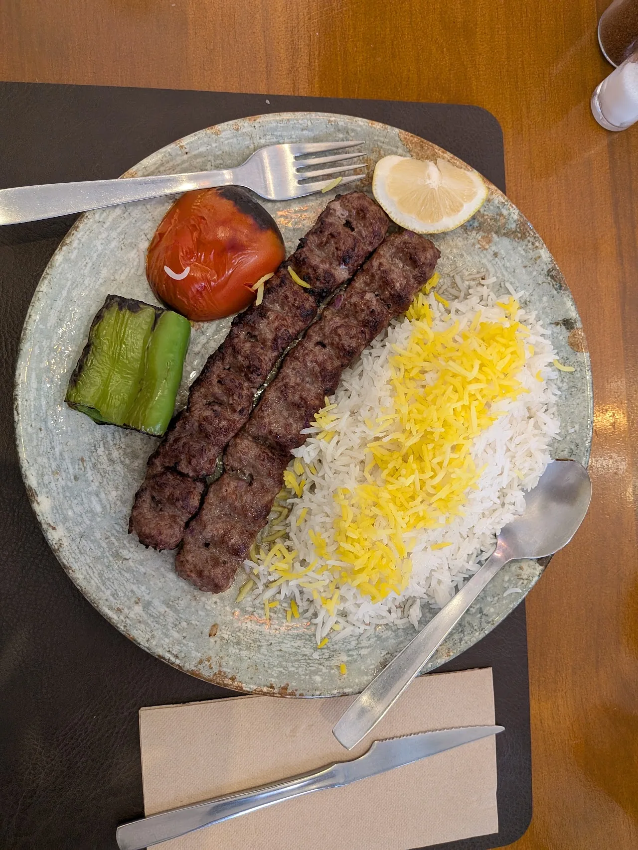 A grilled kebab skewer with saffron rice, tomato, and cucumber