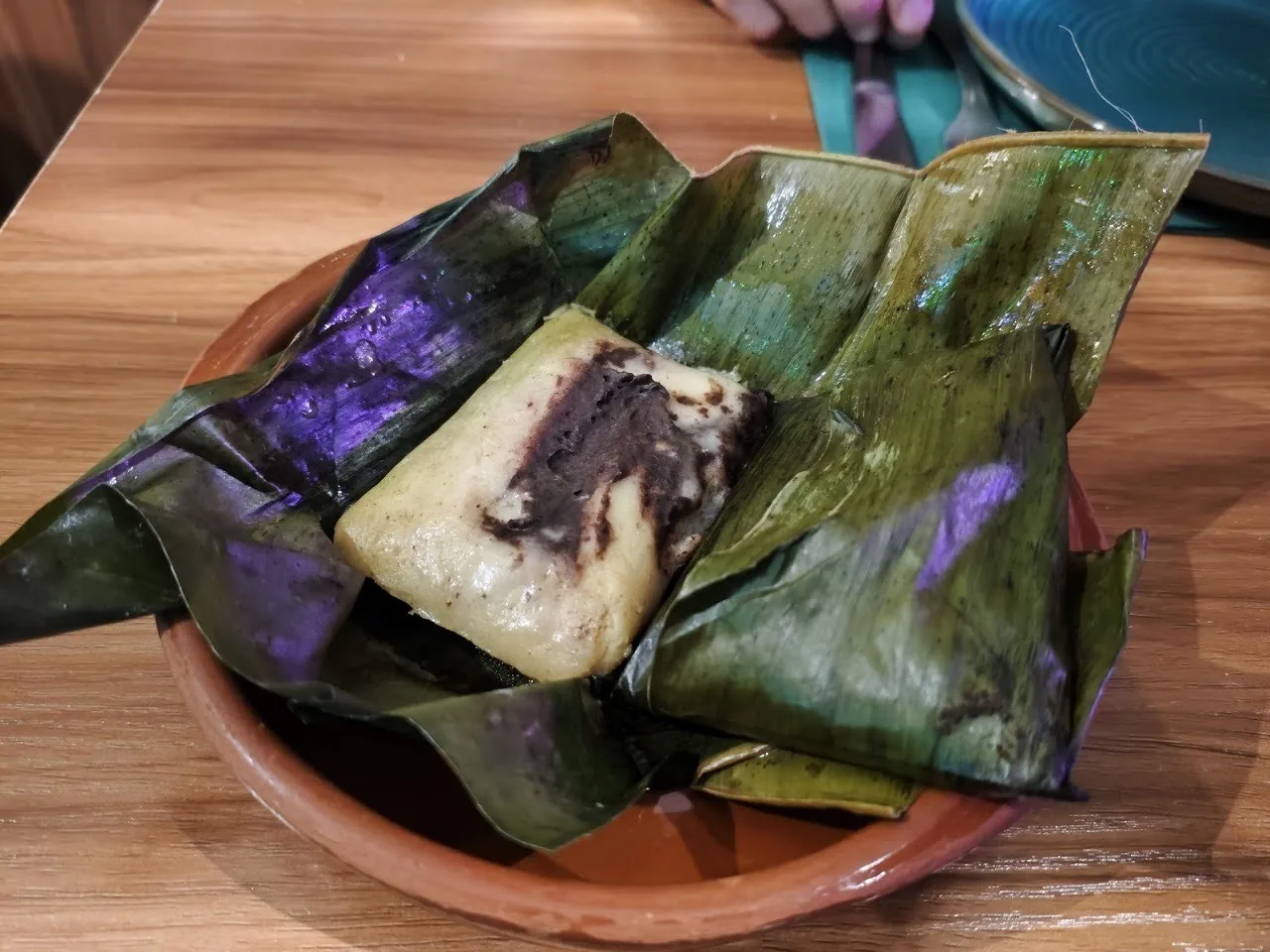Green leaf-wrapped parcels on a terracotta dish, one opened to show a pale filling