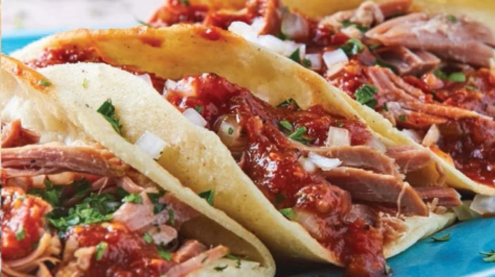Two tacos filled with shredded red meat, chopped onion and herbs