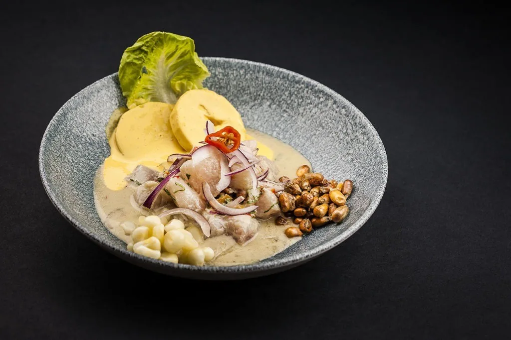 A grey bowl of ceviche with sweet potato and onion slices on a dark surface