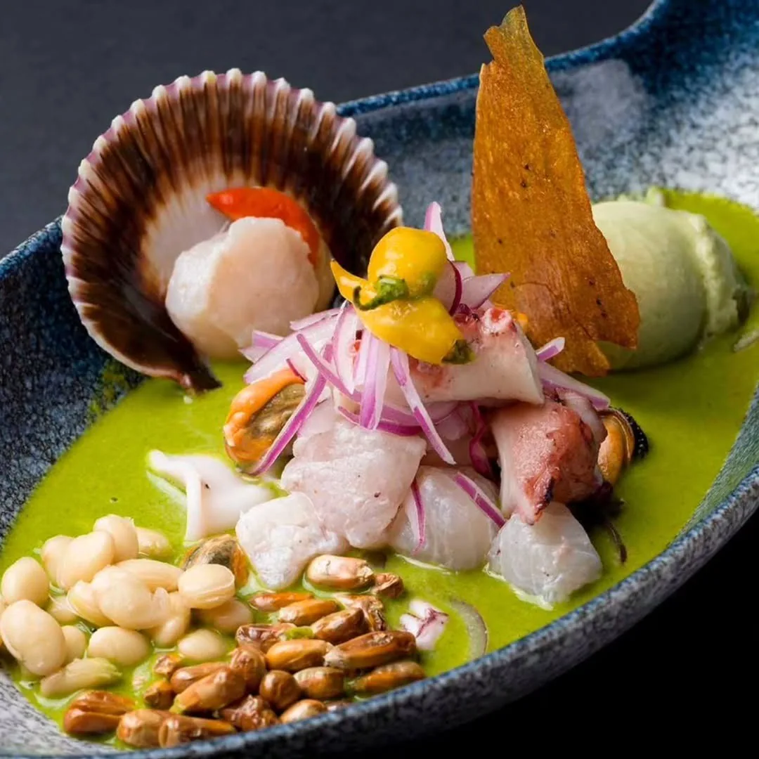 Scallop ceviche with red onion and white beans in a green sauce, served in a dark bowl with a crisp tuile