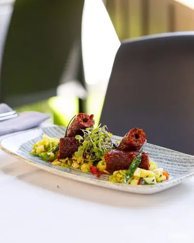Plated tandoori skewered meat pieces over a bed of vegetables topped with microgreens on a speckled rectangular plate
