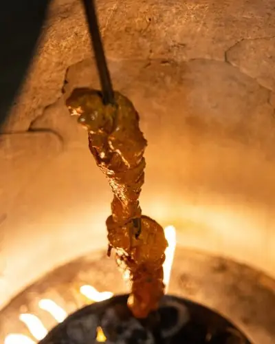 Skewer of glazed chicken tikka cooking inside a glowing clay tandoor oven