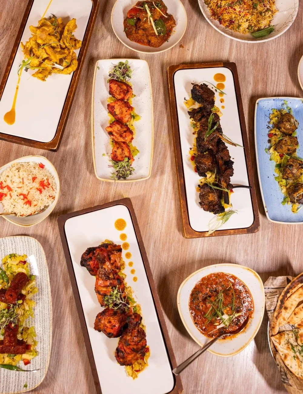 A table seen from above with several long plates of grilled skewers and small bowls of curry and rice