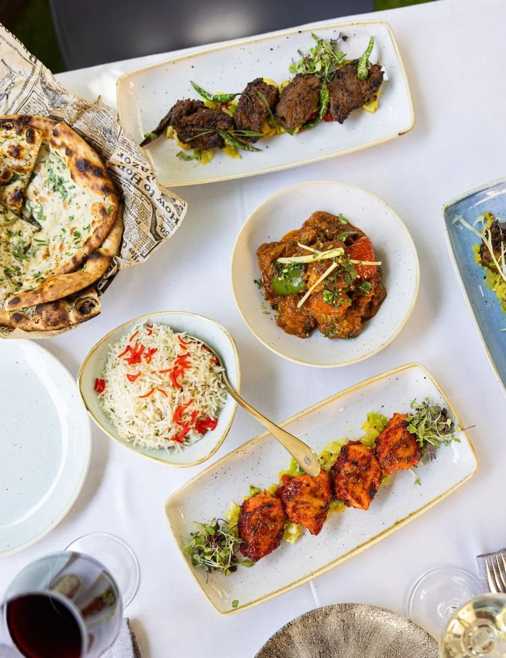 A table seen from above with naan, bowls of curry and rice, and a plate of grilled chicken pieces