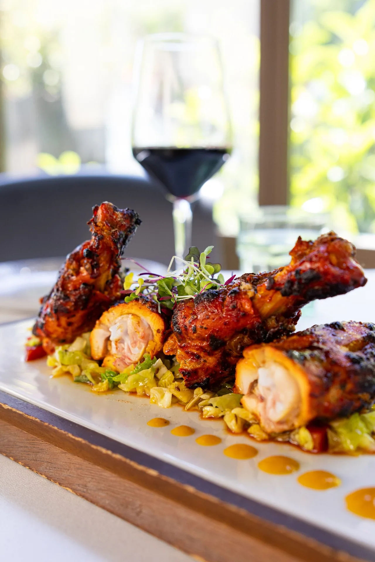 Grilled chicken legs with a golden glaze on a wooden board with a glass of red wine behind
