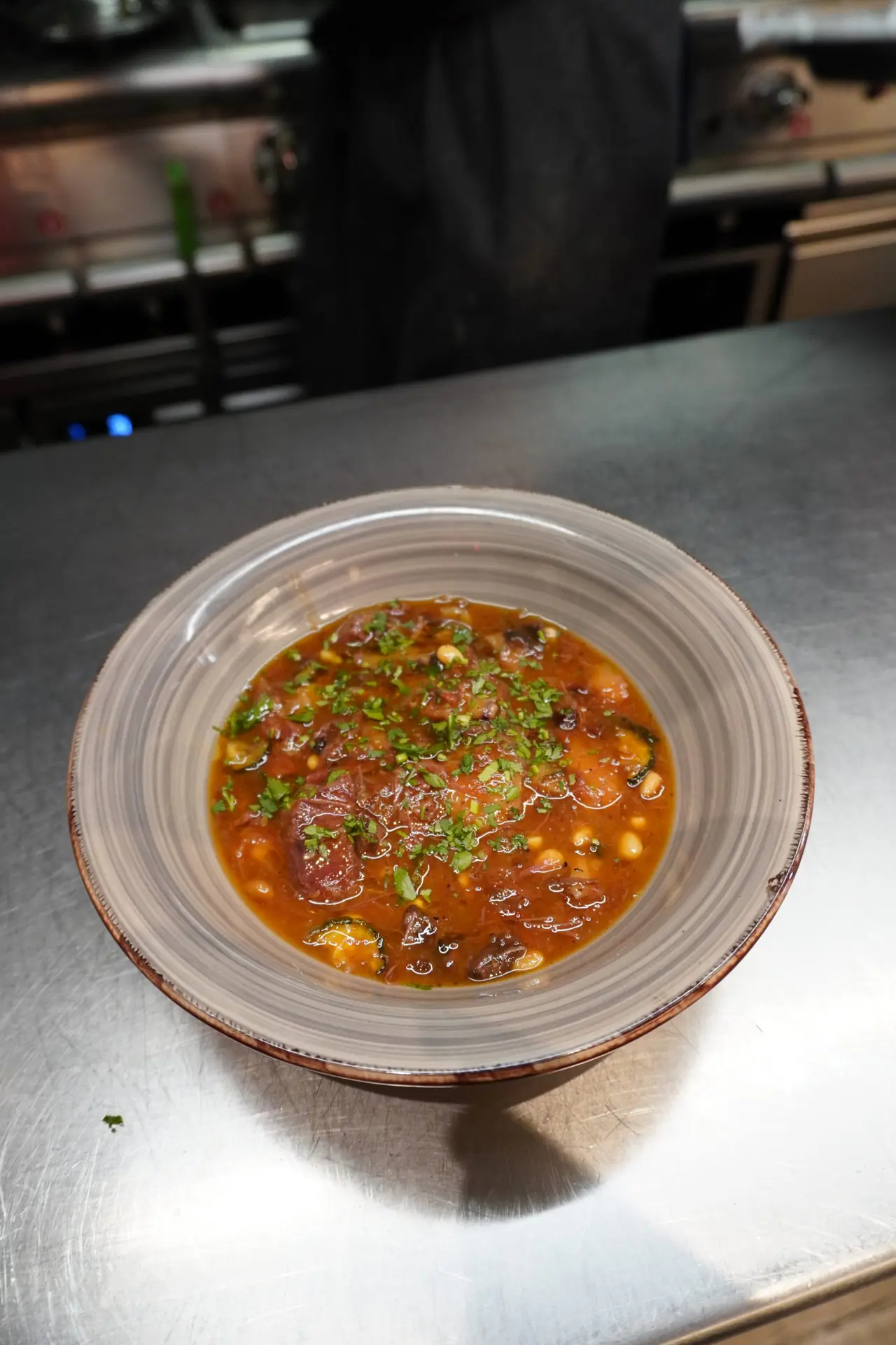 Bowl of slow-cooked meat stew with chickpeas, courgette, and chopped parsley, drizzled with olive oil, at Tangana