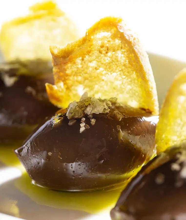 Chocolate-coated olive-shaped dessert topped with a crisp golden wafer and sea salt, drizzled with olive oil, at Tapas 24