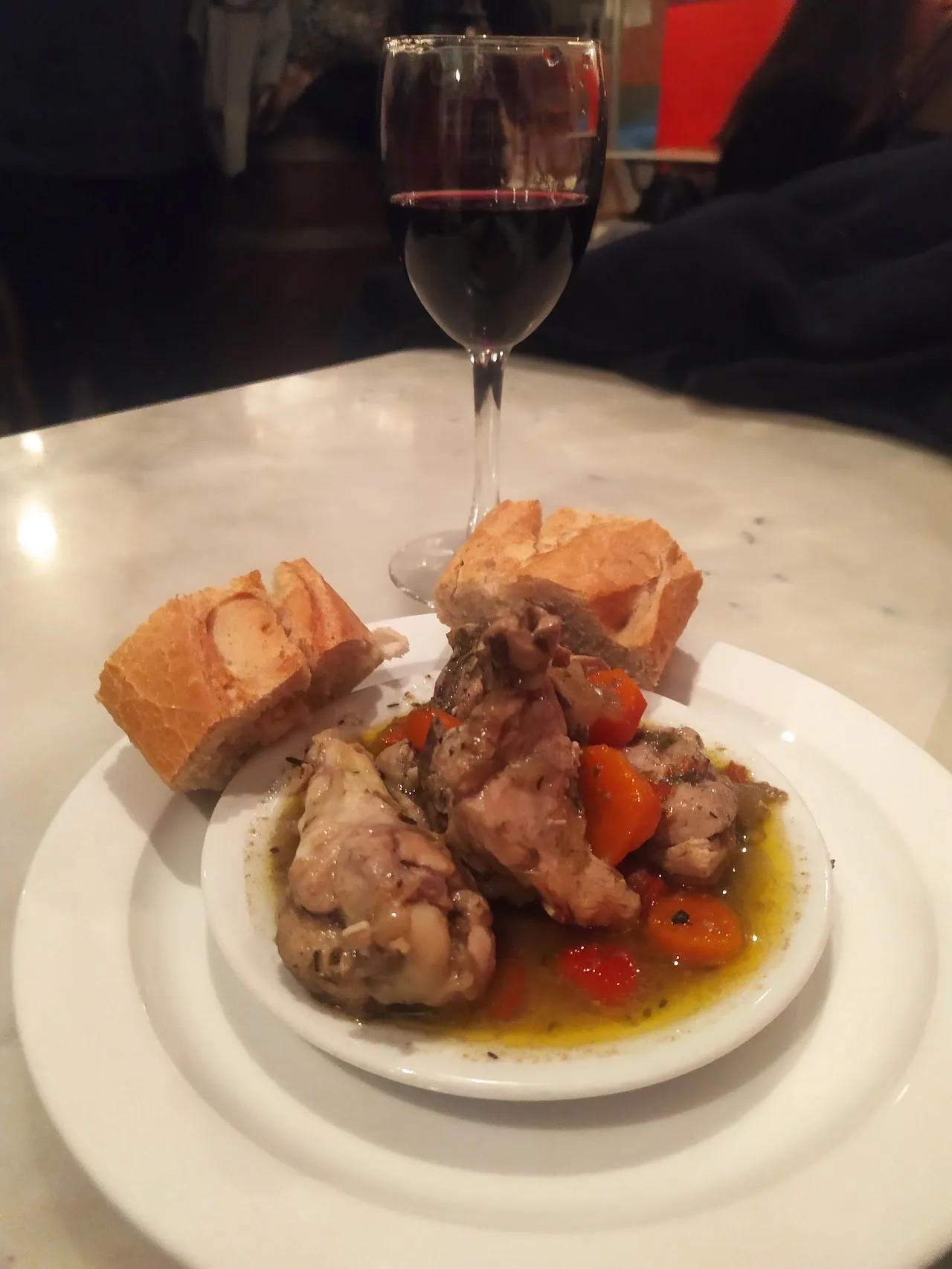 A plate of braised chicken in sauce with bread and a glass of wine