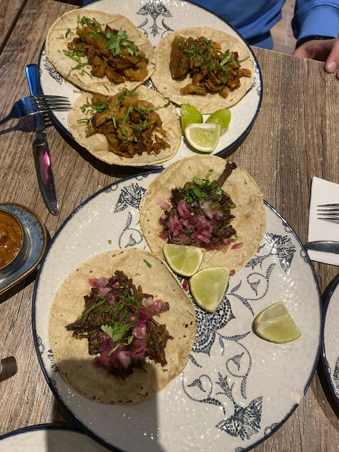 Two plates of soft tacos filled with meat, garnished with lime