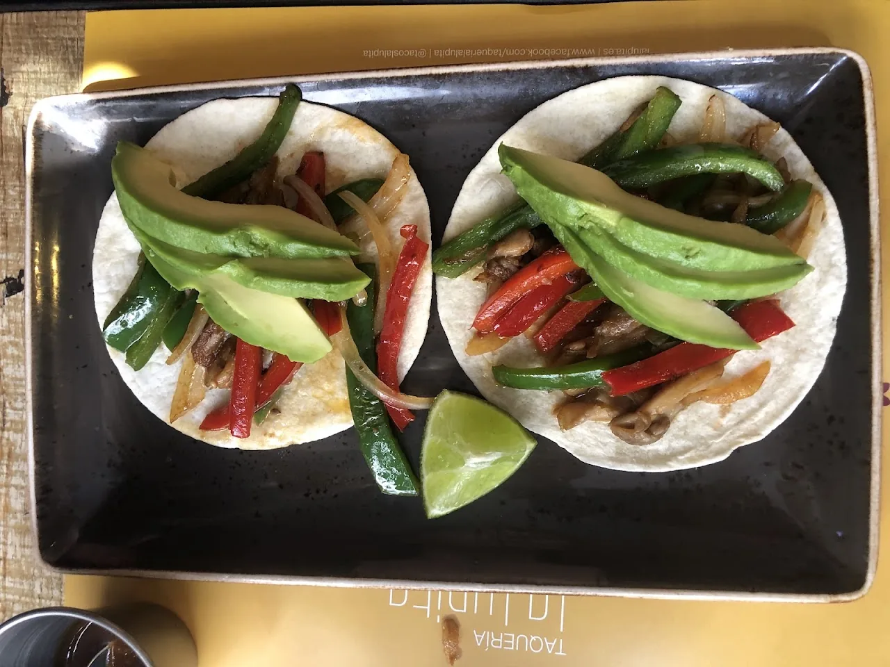 Two soft tacos filled with grilled vegetables and meat, topped with lime