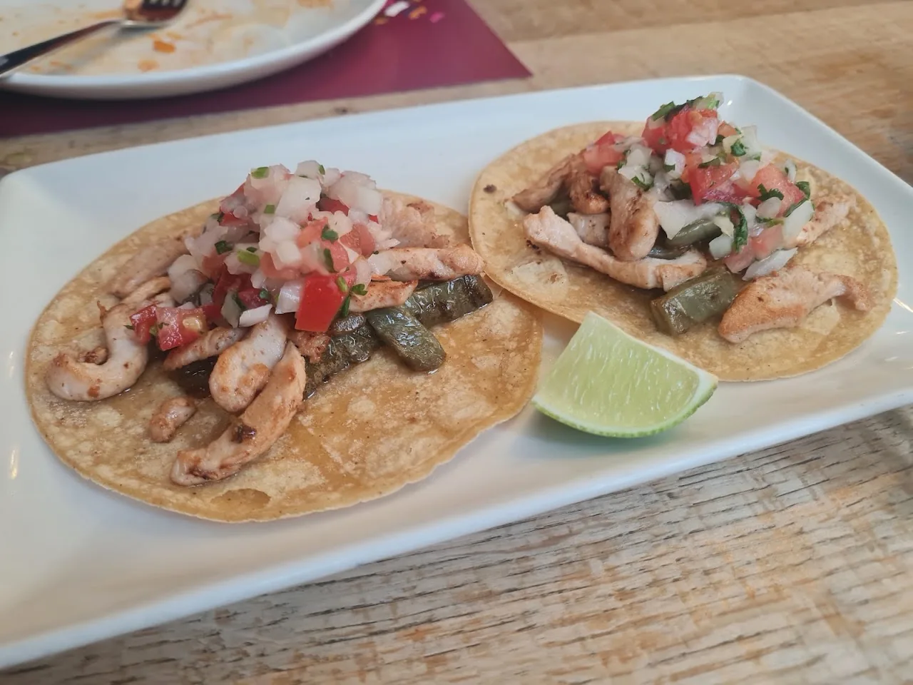 Two tacos topped with shrimp, pico de gallo, and lime