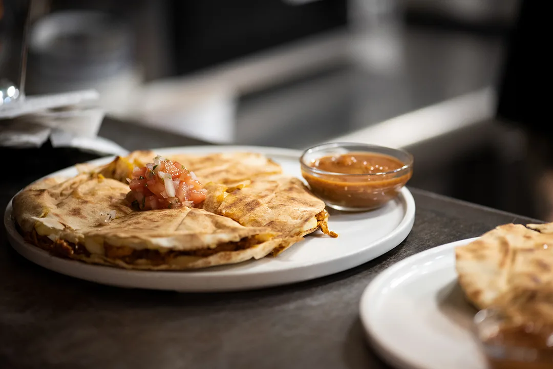 A folded quesadilla with a side of dipping sauce