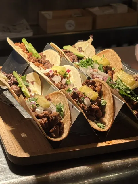 A row of soft-shell tacos filled with meat, avocado, chopped onion, cilantro, and pineapple, served in a wooden holder, at Taquerías Tamarindo