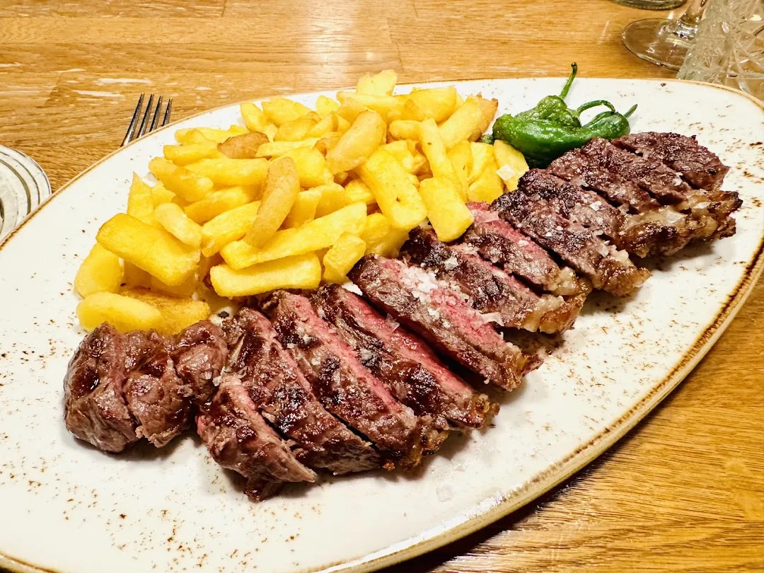 Sliced grilled steak with a side of golden french fries and a grilled green pepper on an oval plate
