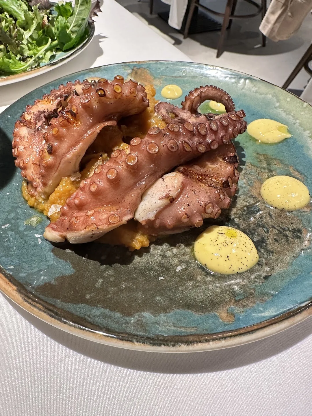 Grilled octopus tentacles on a blue-green plate with dollops of a pale yellow sauce