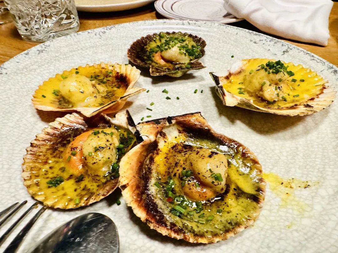 Five grilled scallops in their shells, topped with herbs and a buttery green sauce