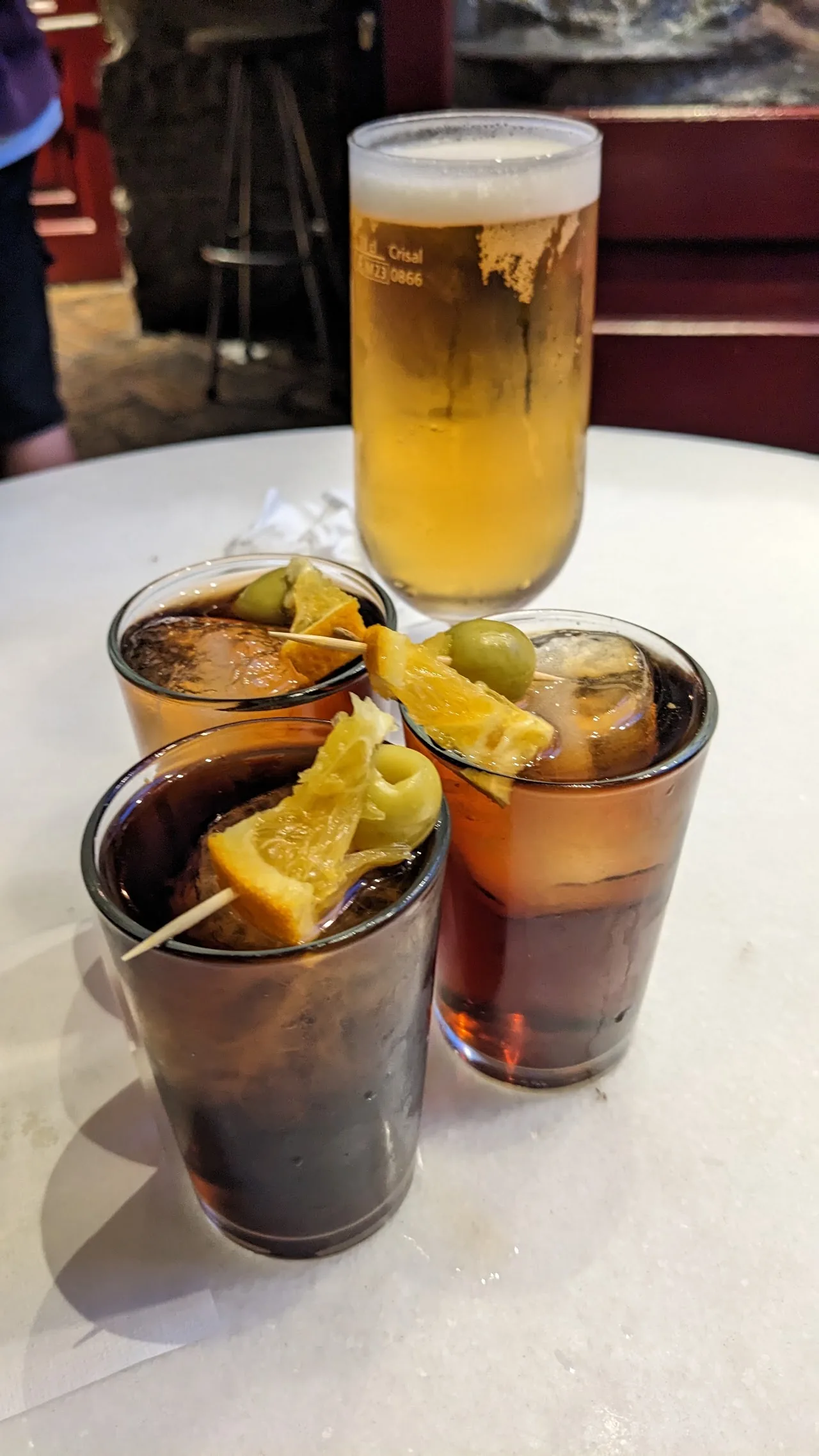 Two glasses of vermouth with orange slices next to a beer