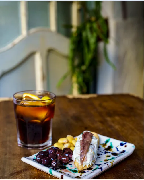 A glass of vermouth on ice with olives beside a plate of toast