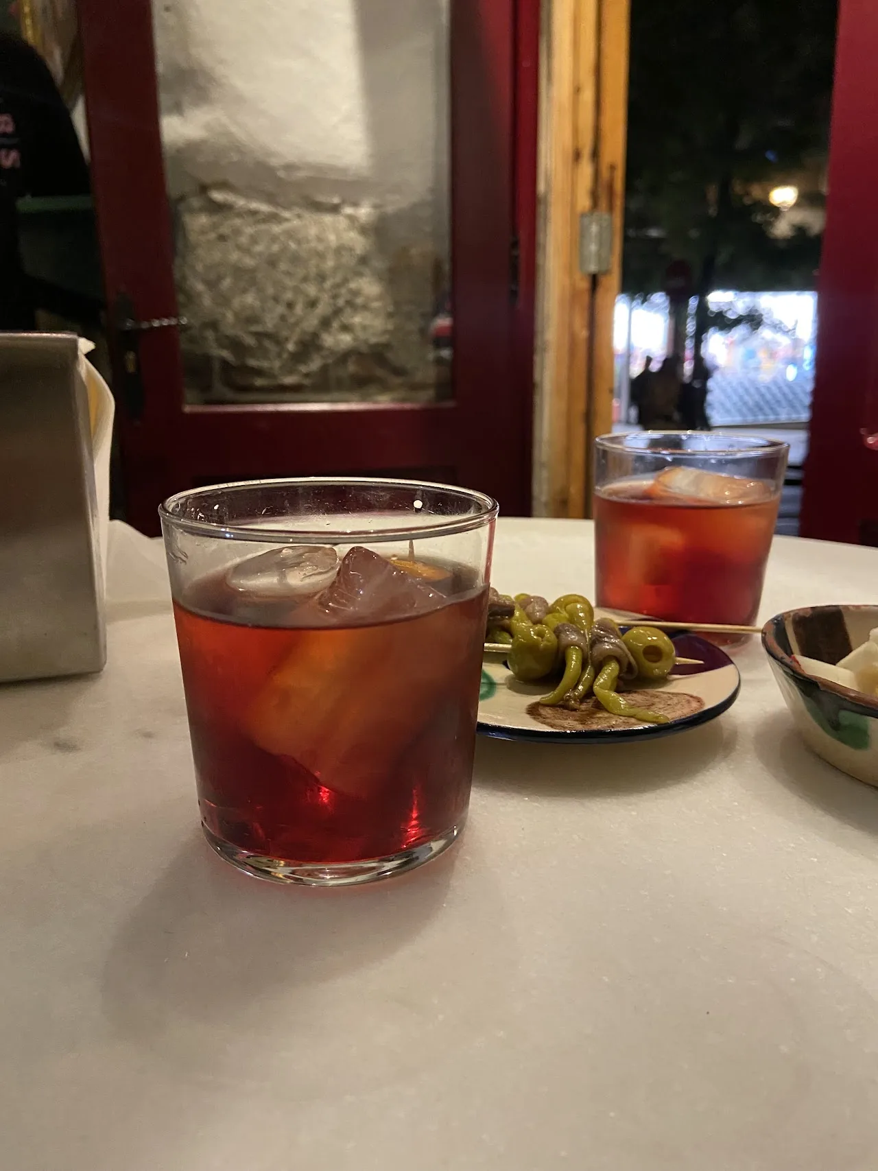 A glass of vermouth on ice with a small dish of pickled guindilla peppers