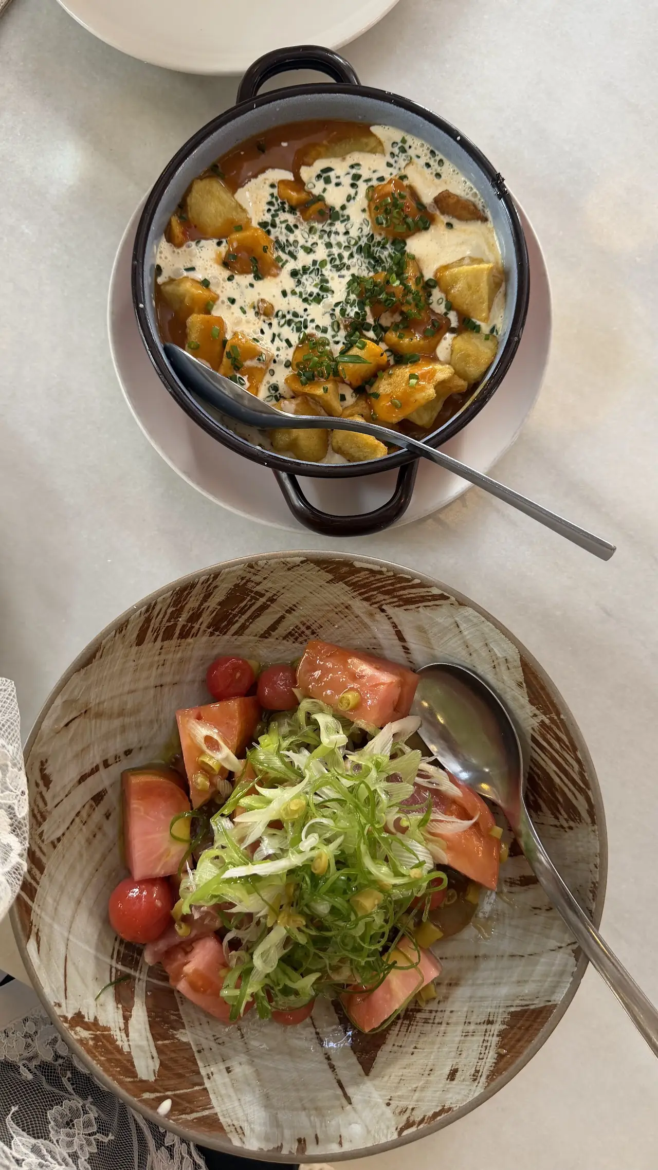 A bowl of sauced potatoes and a plate of sliced tomato salad with onion, viewed from above.