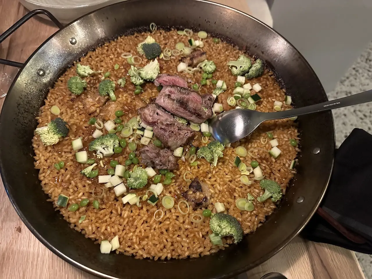 A pan of rice topped with sliced meat, broccoli and diced vegetables.