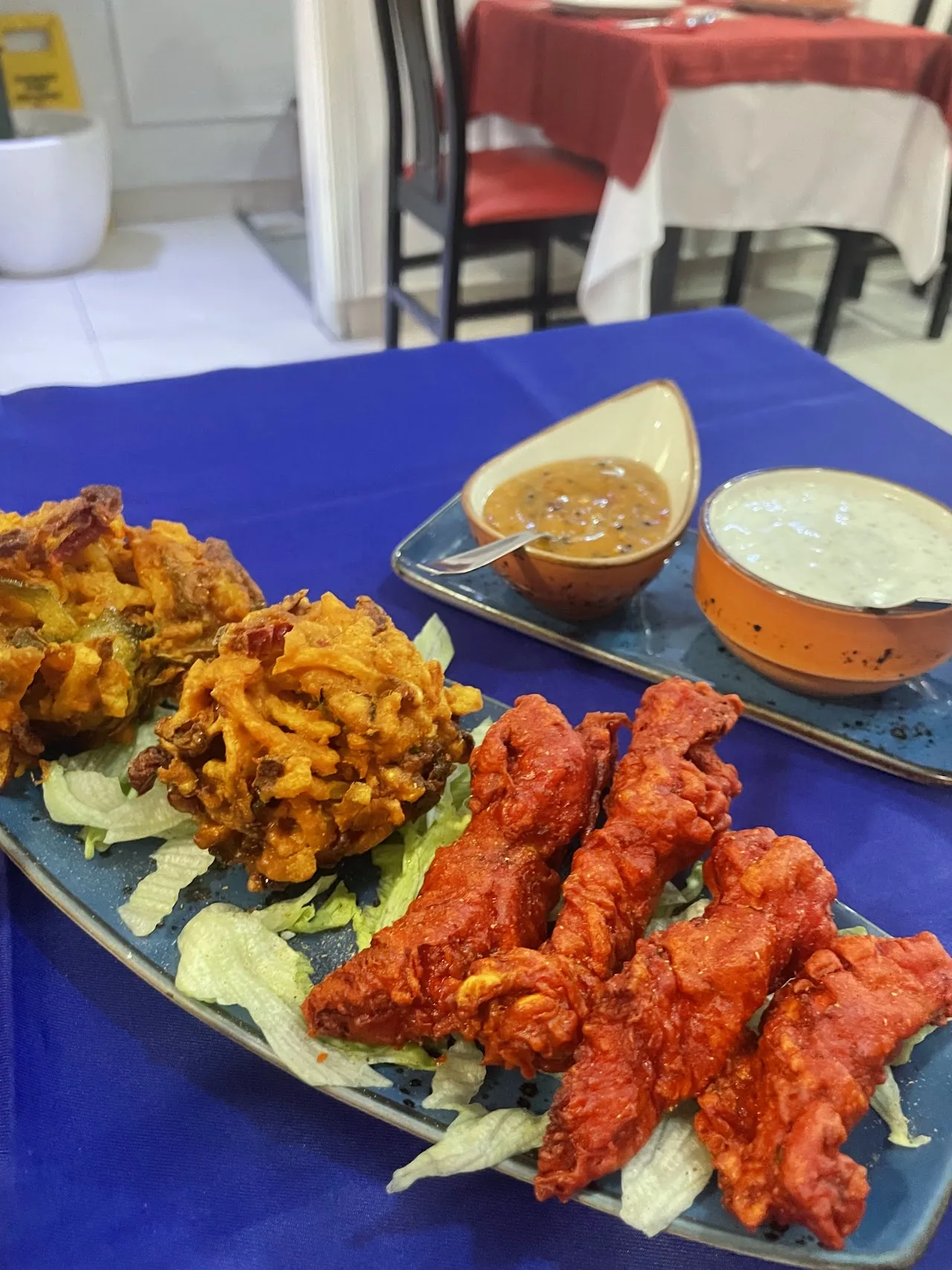 Tandoori chicken and fried pakora on a platter with dipping sauces