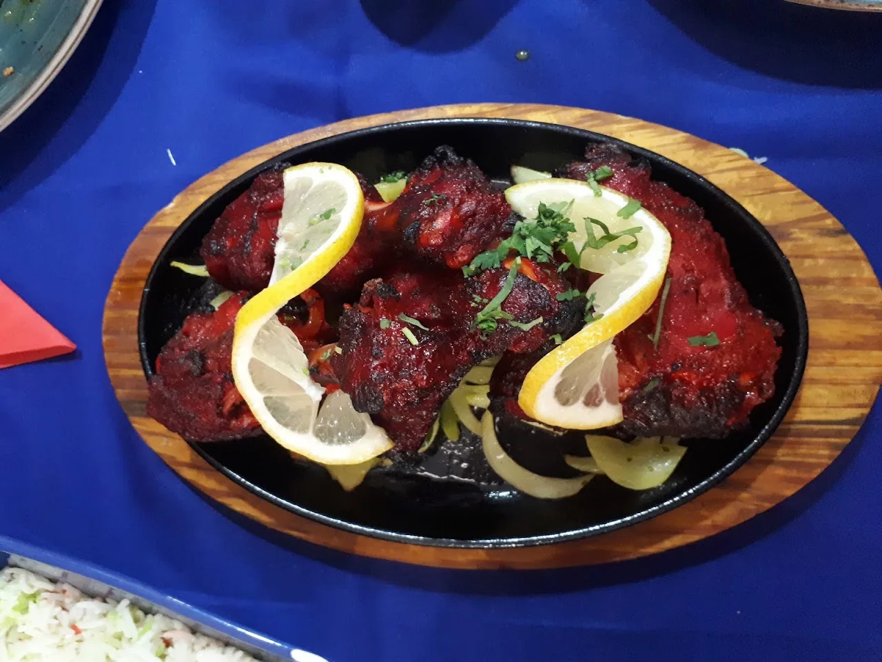 Tandoori chicken pieces on a sizzling plate with lemon