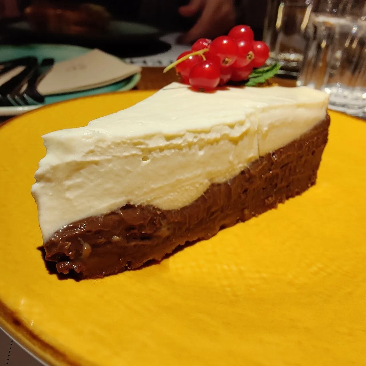 A slice of layered chocolate and cream cake on a yellow plate topped with red berries
