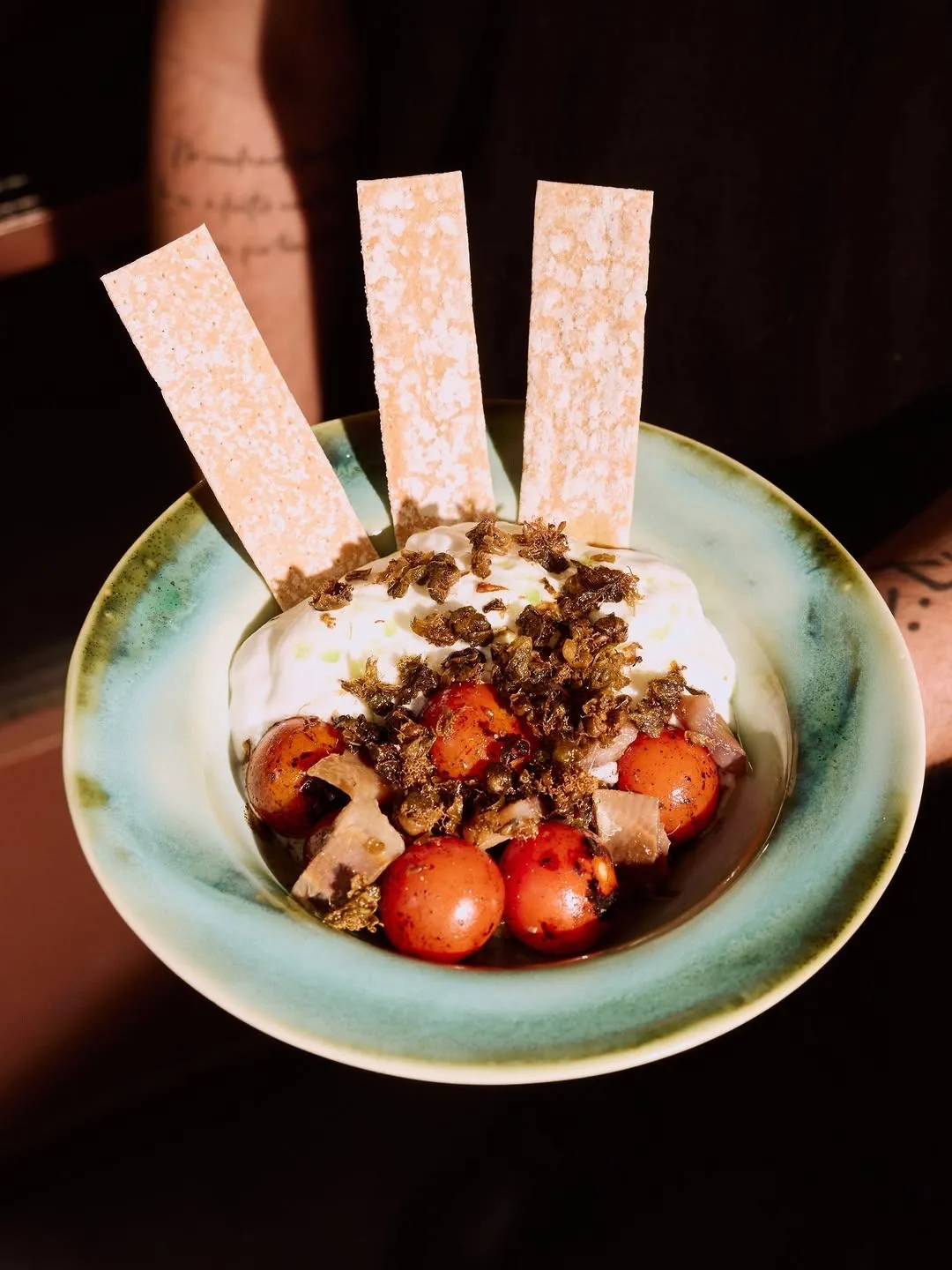 A blue-green bowl of cream topped with crumbled meat, tomatoes and crisp strips