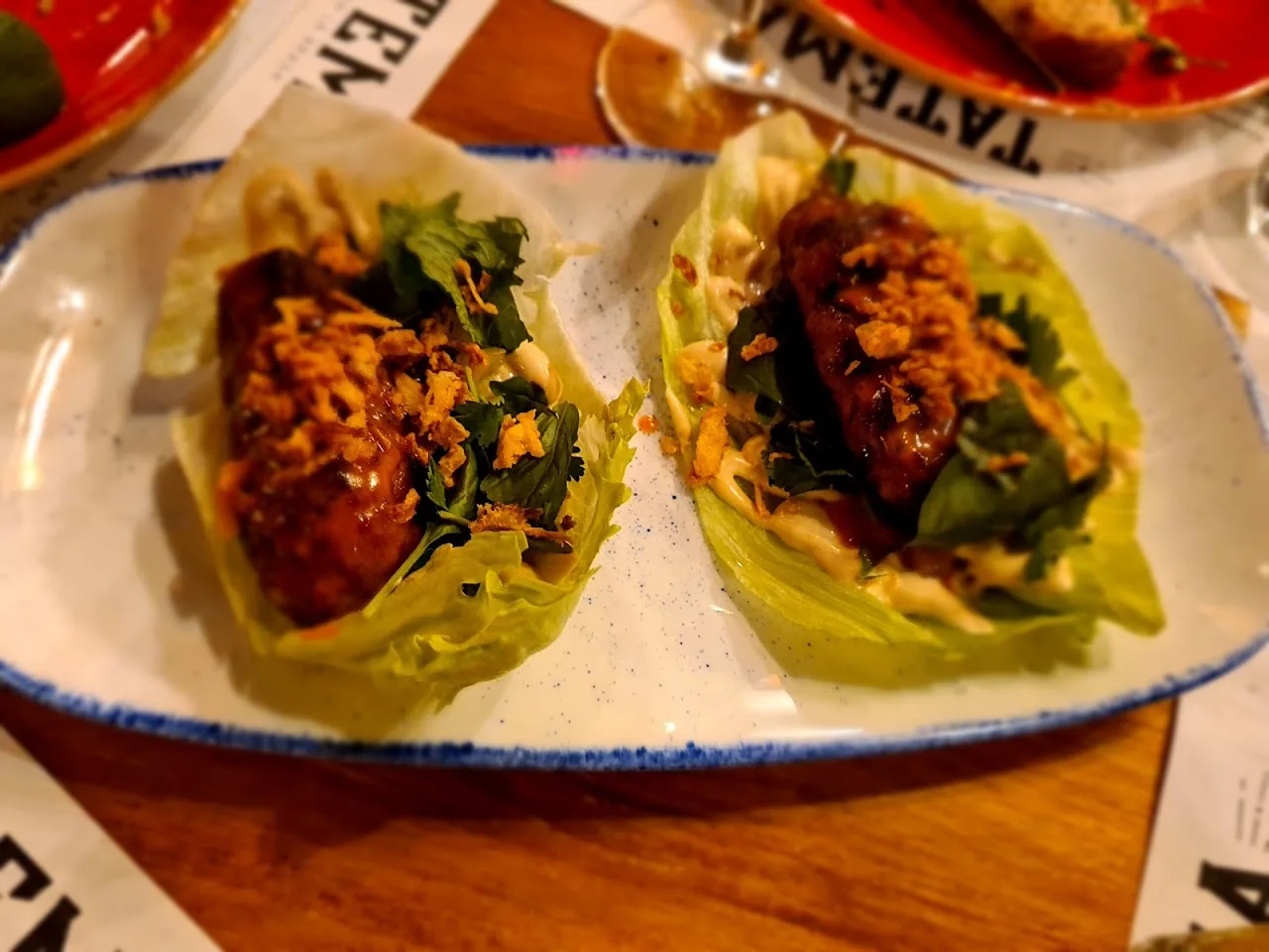 Two lettuce-wrapped tacos topped with charred meat and greens
