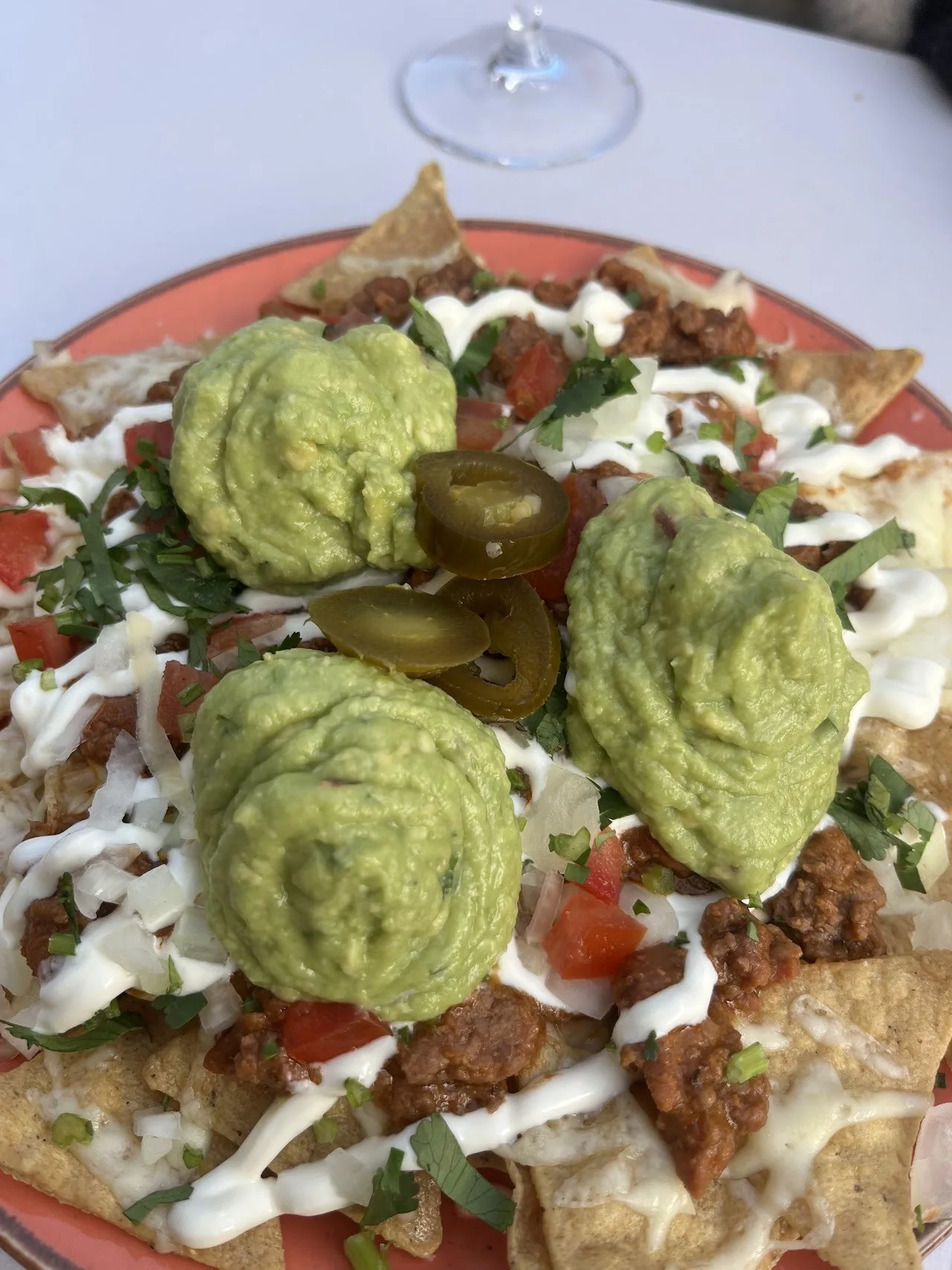 A plate of crisp tortillas topped with scoops of guacamole, cream and sliced jalapeno
