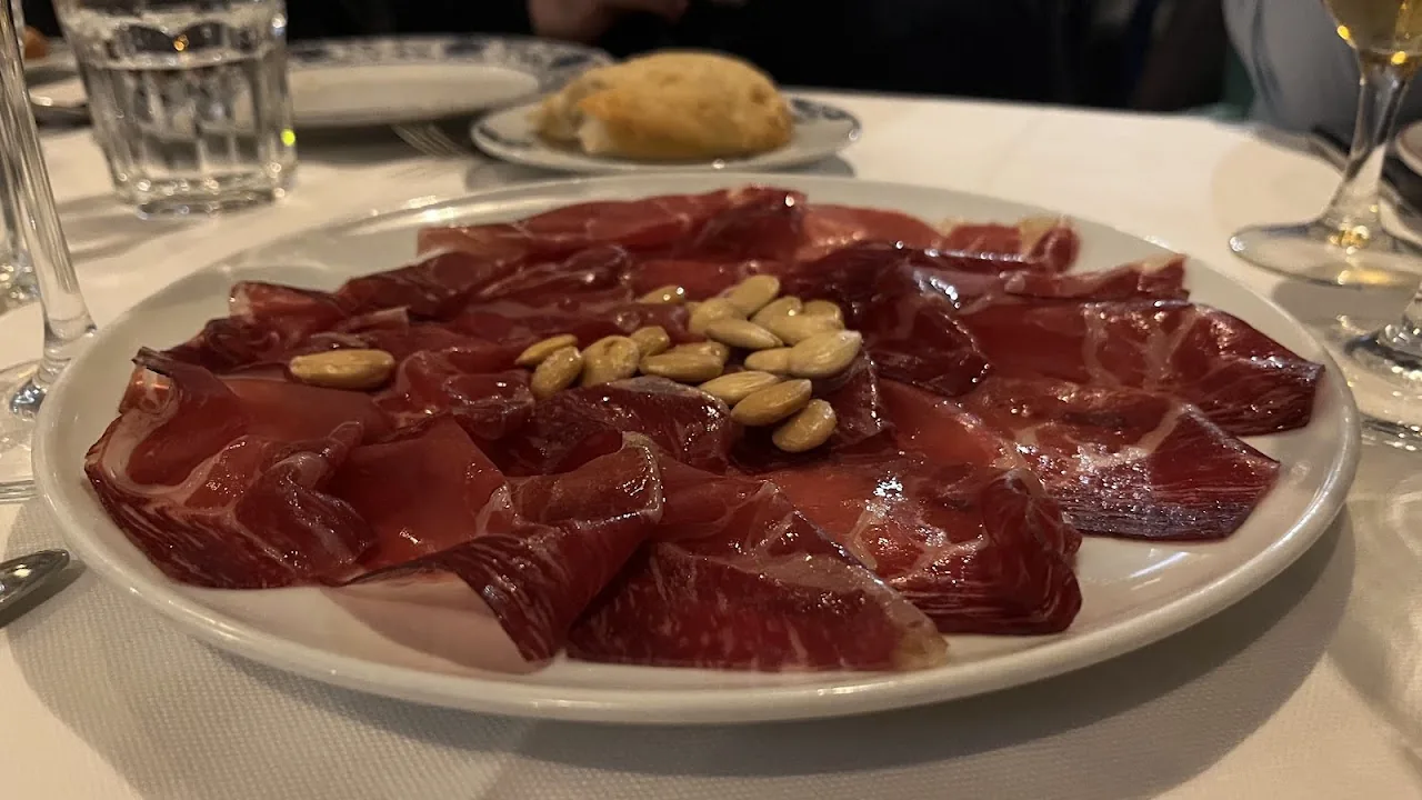 A plate of thinly sliced cured ham with almonds