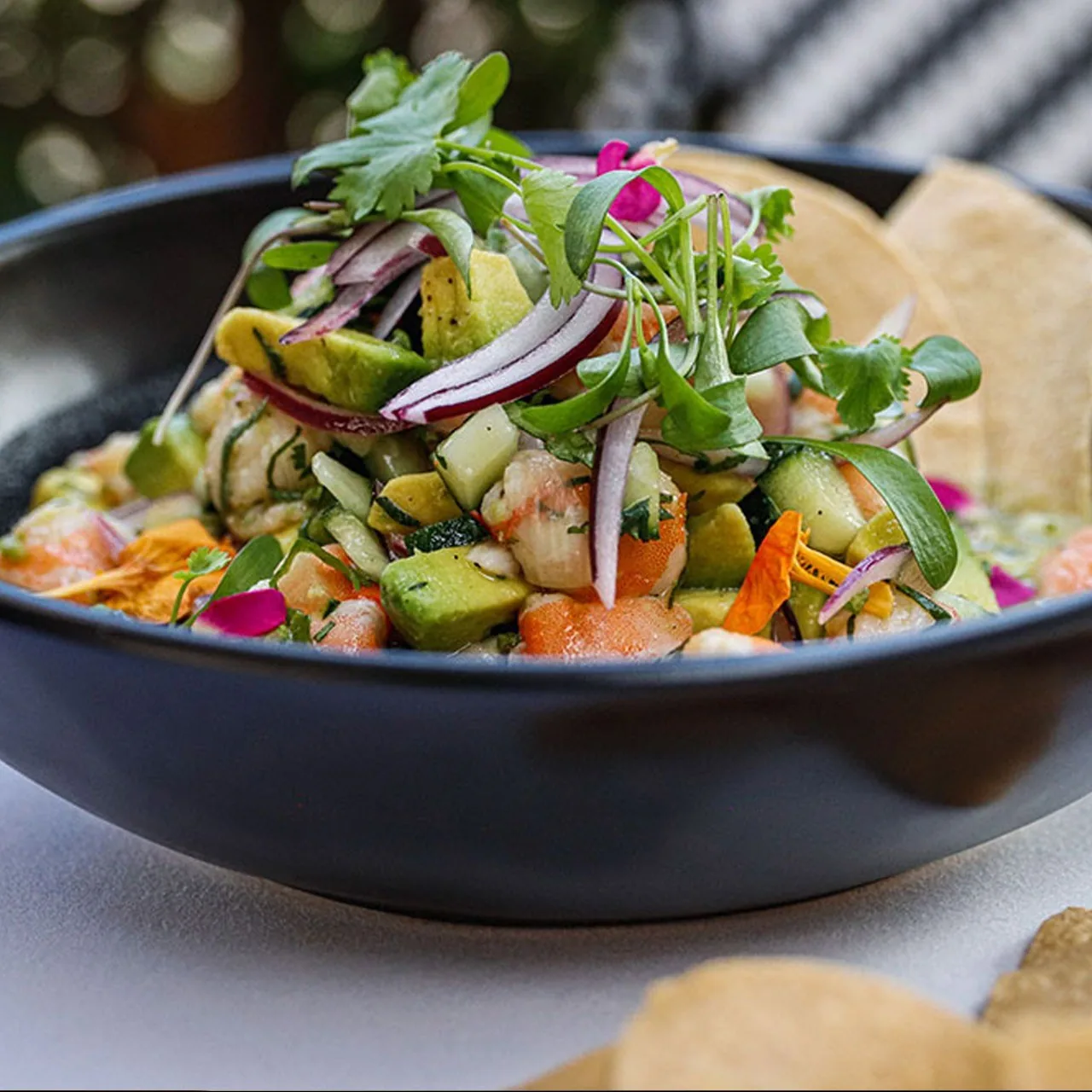 A dark bowl of diced seafood and avocado with red onion and fresh herbs