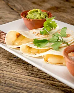A plate of folded quesadillas with a side of guacamole and salsa, garnished with cilantro.