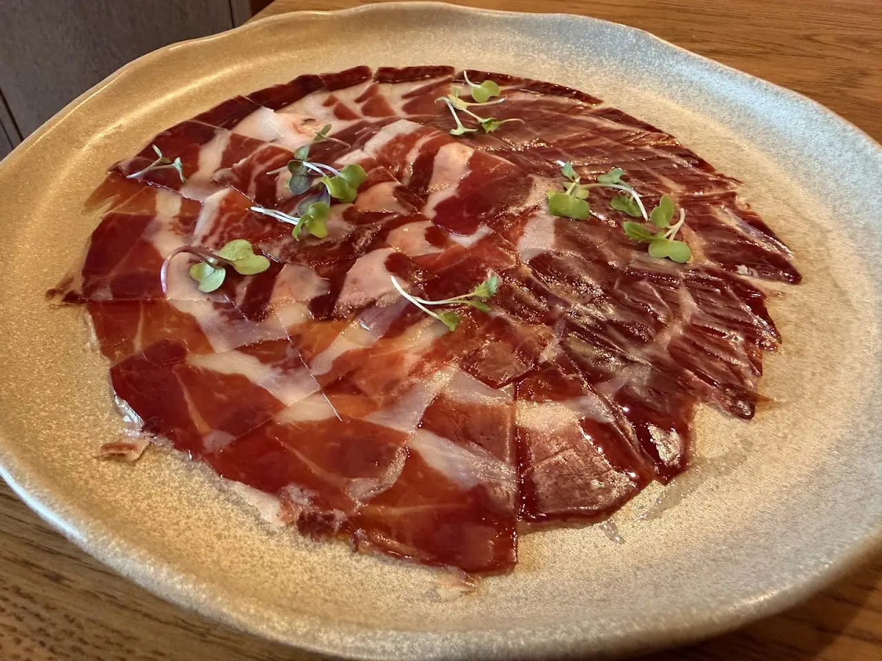 Thinly sliced cured ham fanned out on a large plate with microgreens.