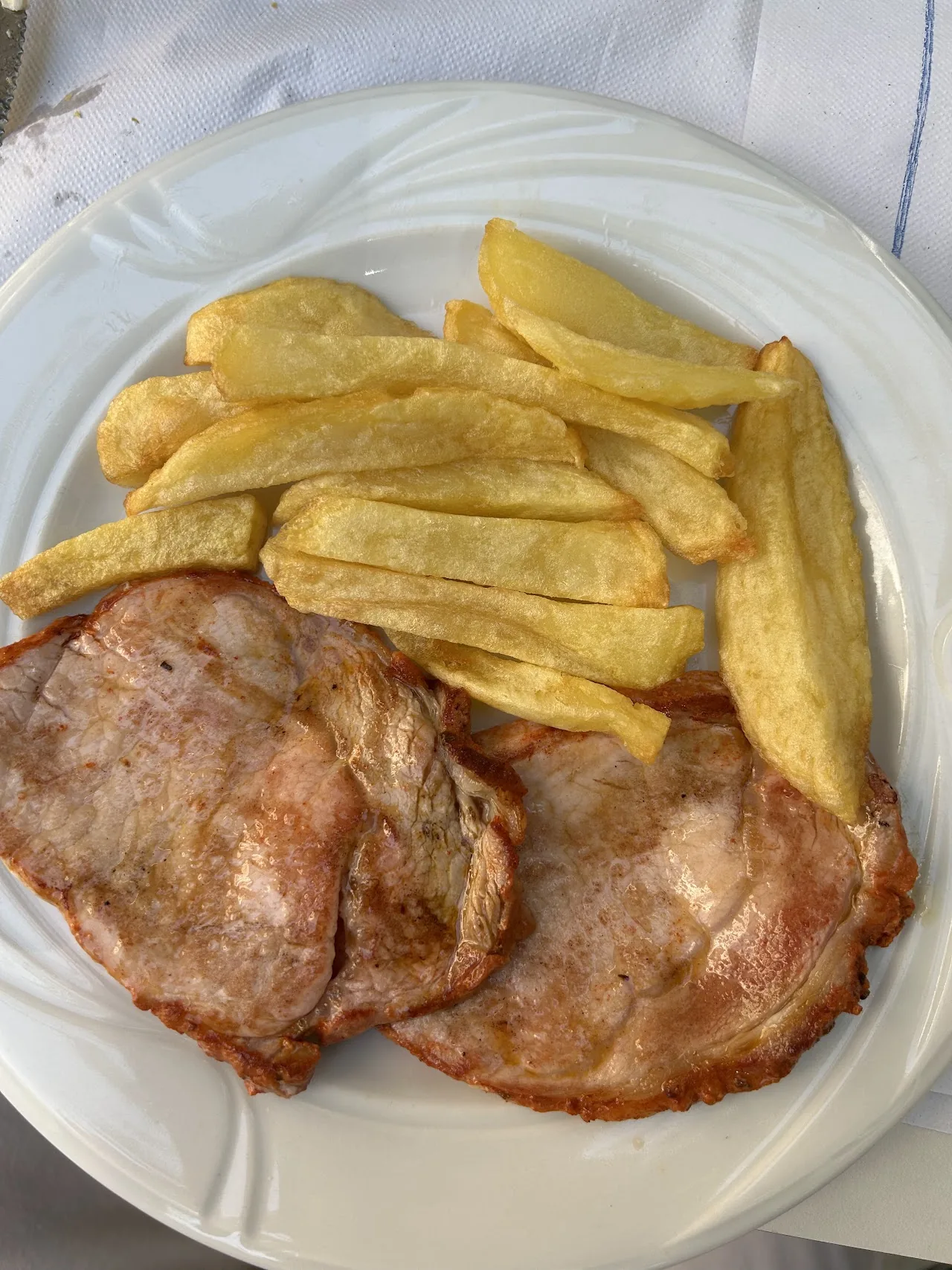 A plate of grilled pork loin steaks with a side of fried potatoes
