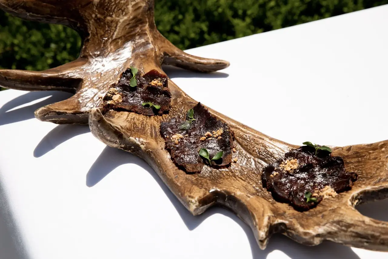 Three dark glazed bites topped with herbs, served along a carved wooden antler board
