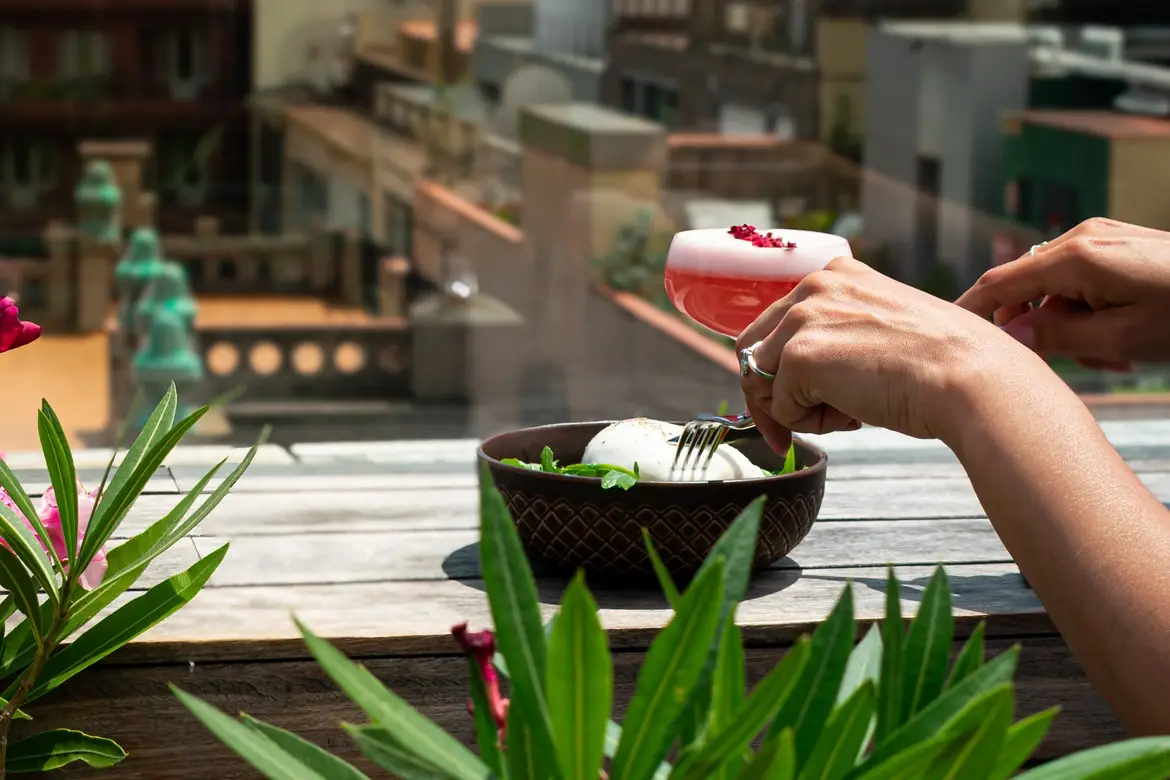 Burrata with mint in a dark ceramic bowl, served alongside a pink cocktail garnished with dried flowers on a rooftop terrace table, Terraza at Sir Victor