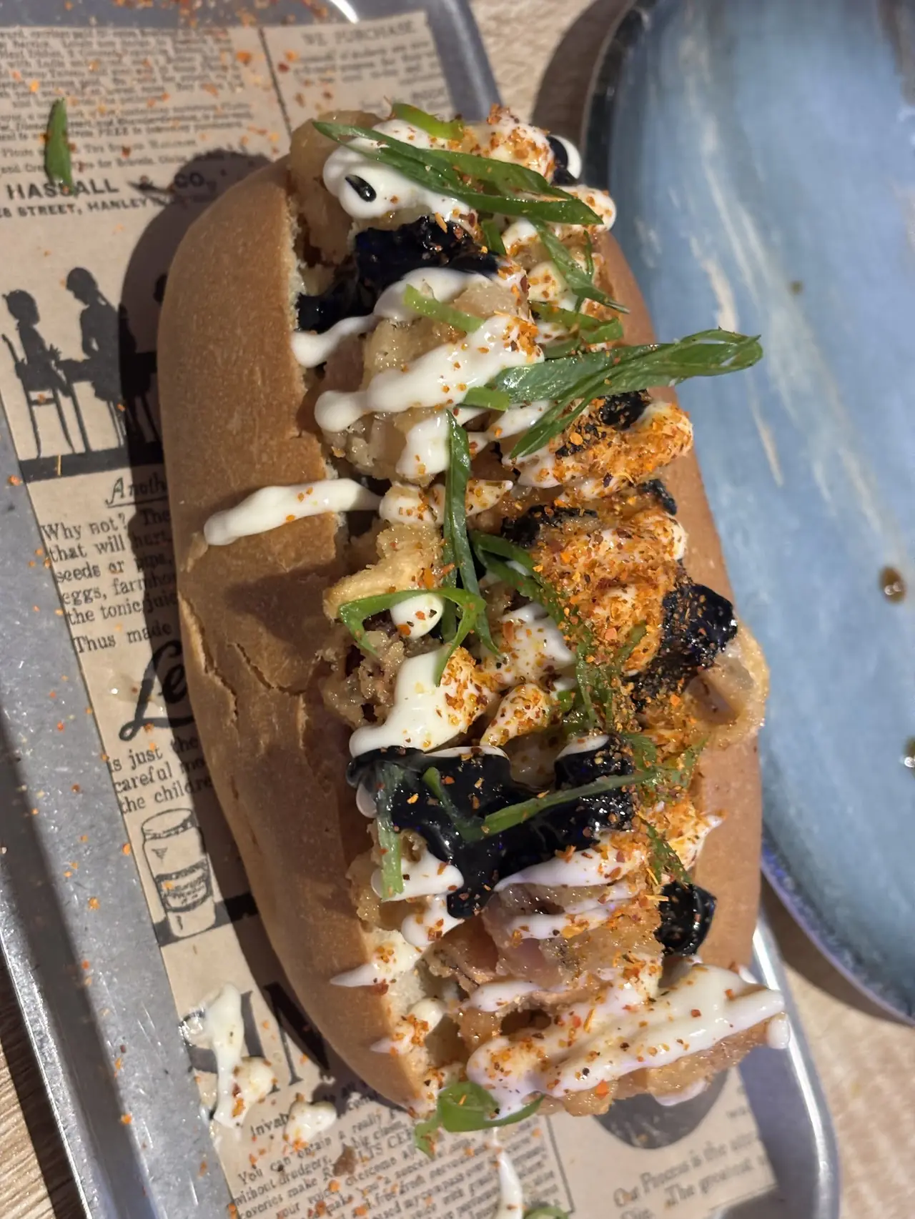 Sandwich roll filled with fried pieces, seaweed and spring onion, drizzled with mayo and chili flakes