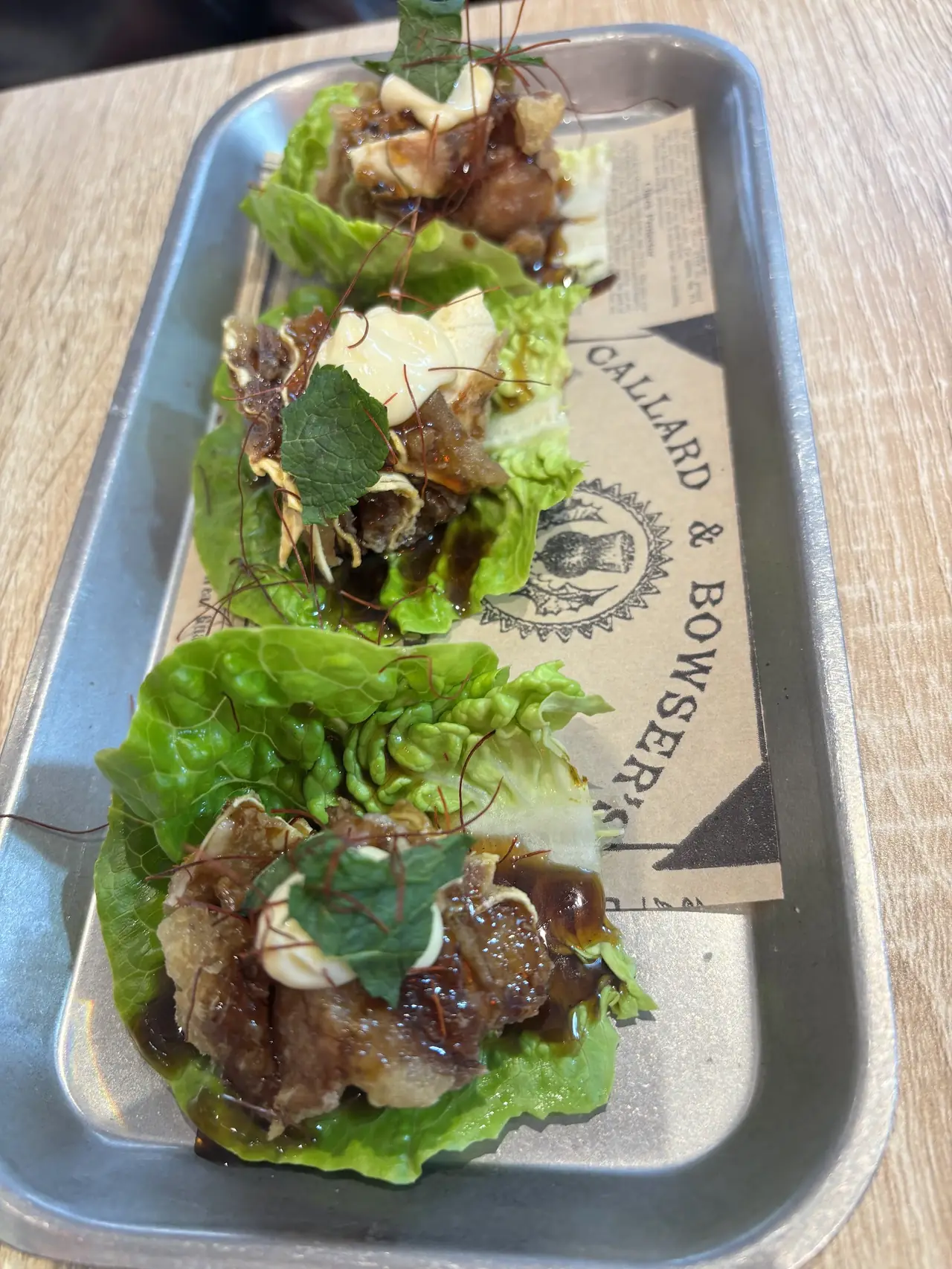 Lettuce cups filled with glazed meat, sauce and mint leaves on a metal tray