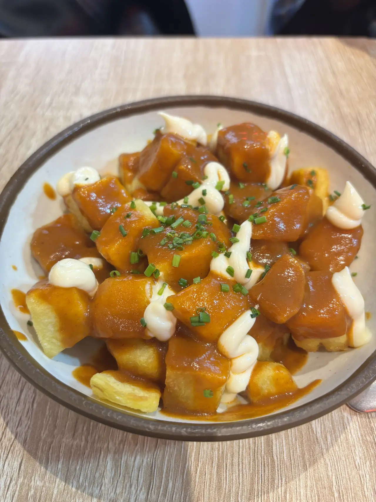 Fried potato cubes in spiced red sauce with dollops of aioli and chopped chives on a plate